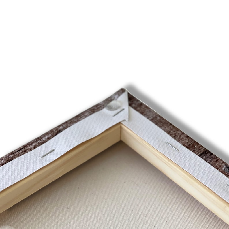 May include: Close-up of the corner of a canvas print stretched over a wooden frame. The canvas is wrapped around the frame and secured with staples. The frame is made of natural wood.