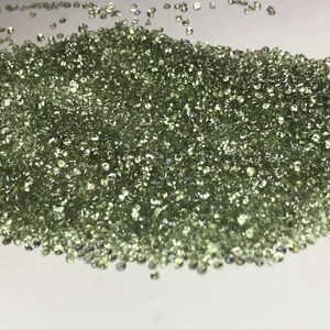 May include: A large pile of small, light green gemstones. The gemstones are round and have a smooth, polished finish.