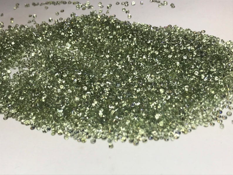 May include: A large pile of small, light green gemstones. The gemstones are round and have a smooth, polished finish.