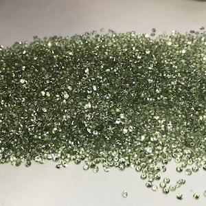 May include: A large pile of small, light green gemstones. The gemstones are round and have a smooth, polished finish.