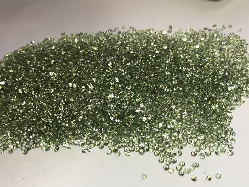 May include: A large pile of small, light green gemstones. The gemstones are round and have a smooth, polished finish.