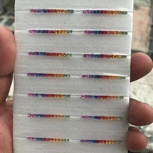 Puede incluir: Una tabla de espuma blanca con filas de pequeñas piedras preciosas cuadradas y coloridas. Las piedras preciosas están dispuestas en filas de diferentes colores, incluyendo azul, verde, amarillo, naranja y rojo.