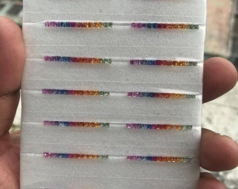 May include: A white foam board with rows of small, square, colorful gemstones. The gemstones are arranged in rows of different colors, including blue, green, yellow, orange, and red.