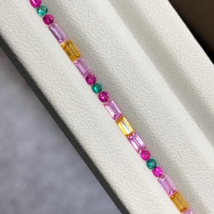 Puede incluir: Una pulsera de piedras preciosas multicolor con un patrón repetitivo de zafiros amarillos y rosas de corte baguette rectangular, intercalados con piedras redondas de color verde vibrante y rosa intenso en una disposición lineal.