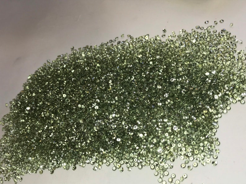 May include: A large pile of small, round, light green gemstones.
