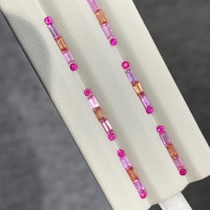 Può includere: Un paio di orecchini lineari con pietre preziose alternate a taglio rotondo e baguette in tonalità rosa e arancione. Ogni orecchino è composto da quattro pietre rotonde rosa e tre pietre rettangolari a baguette in un motivo verticale.