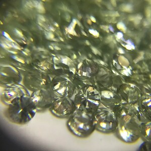 May include: A close-up view of a pile of small, round, faceted green gemstones. The gemstones are translucent and have a slight shimmer.