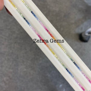 May include: Three strands of colorful gemstones arranged in a rainbow pattern on a white surface. The gemstones are small and round, and they are arranged in a line. The text "Zehra Gems" is visible in the image.