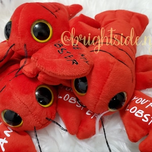 K&ouml;nnte beinhalten: Vier rote Pl&uuml;sch-Hummer-Spielzeuge mit Glitz Augen und dem Text "You're my lobster" auf einem der Hummer.