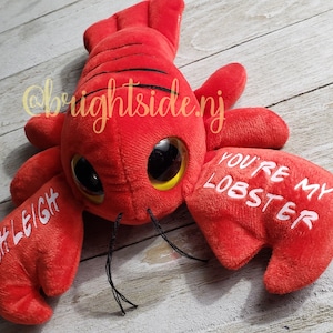 K&ouml;nnte beinhalten: Roter Pl&uuml;sch-Hummer mit Glitz Augen und dem Text "You're my lobster" auf einer Kralle und "Ashleigh" auf der anderen Kralle.