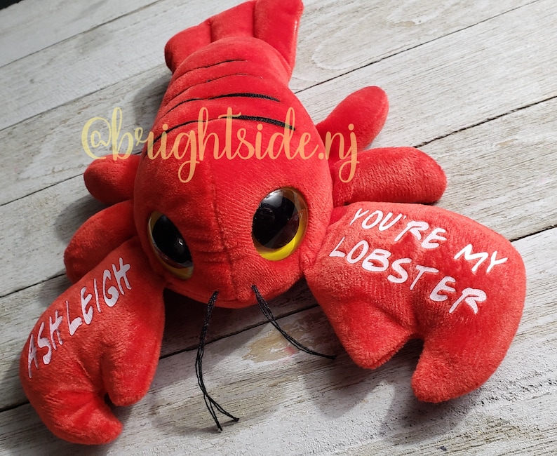 K&ouml;nnte beinhalten: Roter Pl&uuml;sch-Hummer mit Glitz Augen und dem Text "You're my lobster" auf einer Kralle und "Ashleigh" auf der anderen Kralle.