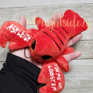 K&ouml;nnte beinhalten: Rotes Pl&uuml;sch-Hummer-Spielzeug mit Glitz Augen und dem Text "You're my lobster" und "Ashleigh" auf den Scheren.