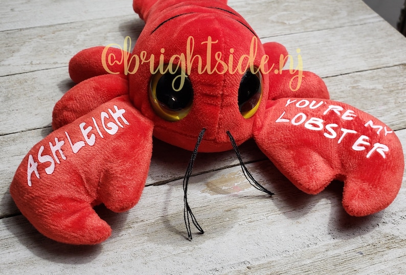 K&ouml;nnte beinhalten: Roter Pl&uuml;sch-Hummer mit Glitz Augen und dem Text "You're my lobster" auf einer Kralle und "Ashleigh" auf der anderen Kralle.