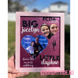May include: A pink framed photo collage with glitter background. The collage includes two photos of young girls, the text "BIG jocelyn" and "LITTLE daphne", and the phrase "dance like no one's watching". The text "FCDA 2025" is also visible.