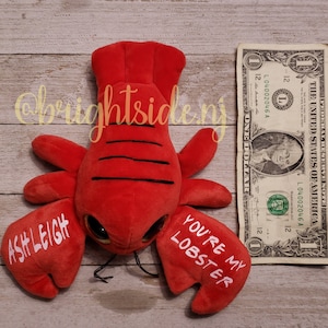 K&ouml;nnte beinhalten: Rotes Pl&uuml;sch-Hummer-Spielzeug mit Glitz Augen und dem Text "You're my lobster" und "Ashleigh" auf den Scheren.
