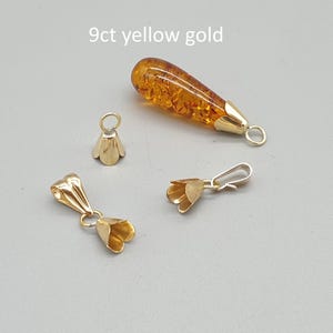 May include: A collection of 9ct yellow gold jewelry components including three bell-shaped pendant bails and one teardrop-shaped amber pendant with a gold cap. The text 9ct yellow gold is visible at the top of the image, indicating the material.