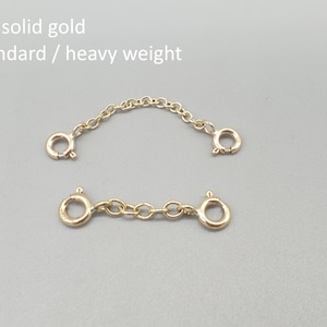 May include: Two gold-colored chain extenders with clasp closures. The top extender is curved, and the bottom one is straight. The text "9ct solid gold standard / heavy weight" is in the upper left corner.