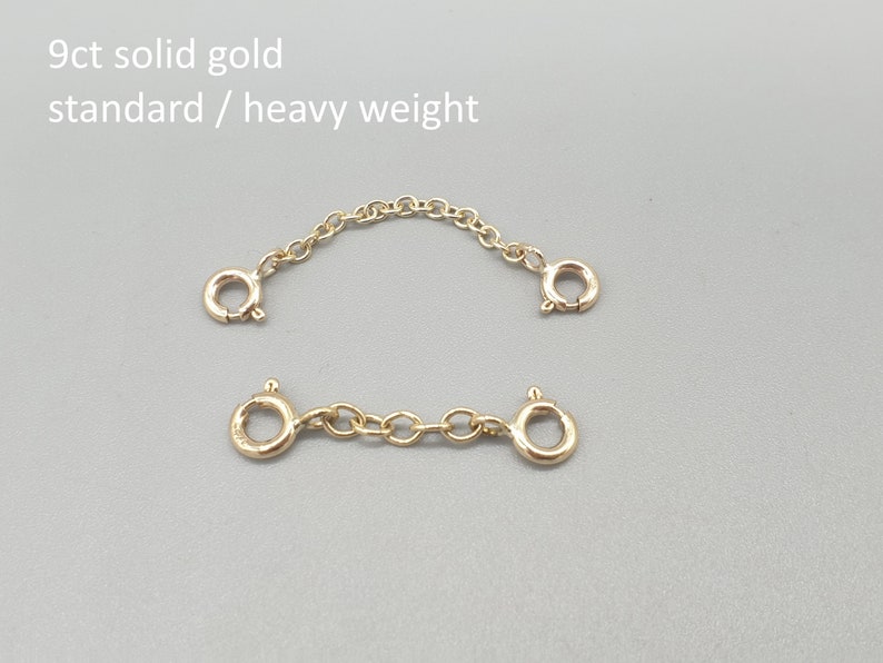 May include: Two gold-colored chain extenders with clasp closures. The top extender is curved, and the bottom one is straight. The text "9ct solid gold standard / heavy weight" is in the upper left corner.
