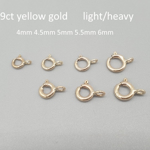 Pode incluir: Várias fechos de mola em ouro amarelo 9ct em vários tamanhos: 4 mm, 4,5 mm, 5 mm, 5,5 mm e 6 mm. Os fechos estão dispostos sobre uma superfície cinza claro. O texto na imagem diz "9ct yellow gold light/heavy".