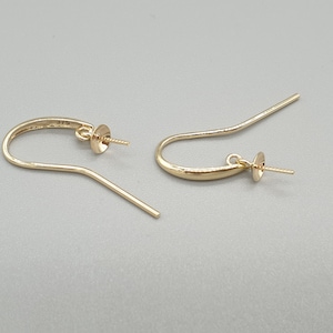 May include: Two gold-coloured earring hooks, each with a curved design and a small post for attaching a bead or charm. The hooks have a simple, elegant style, ideal for DIY jewellery projects or adding to existing earrings.