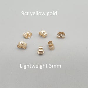 May include: Five small 9ct yellow gold earring backs, each measuring 3mm in diameter. These lightweight, circular metal components feature a central hole for securing earring posts, presented with the text 9ct yellow gold and Lightweight 3mm.