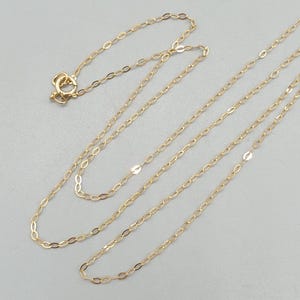 May include: A delicate gold chain necklace featuring elongated oval links. The necklace includes a small circular spring ring clasp at one end, allowing for secure fastening. The chain is composed of thin, polished gold metal links.