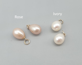 May include: Close-up of four pearl pendants in rose and ivory colors. The rose-colored pearls have a pink hue, while the ivory pearls are white. Each pearl is attached to a small gold-colored loop.