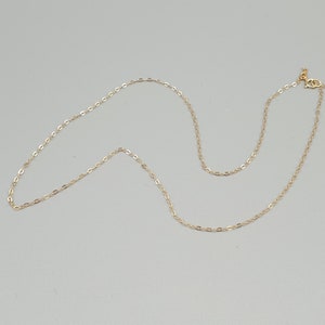 May include: A delicate gold chain necklace featuring small, uniform oval-shaped links. The necklace is finished with a small, circular spring ring clasp at one end, providing a secure closure for this simple and refined piece of jewellery.