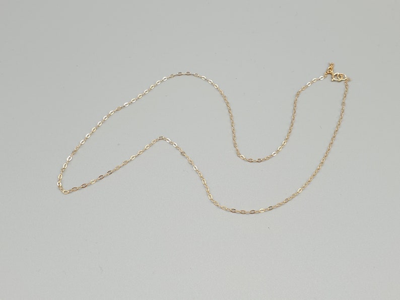 May include: A delicate gold chain necklace featuring small, uniform oval-shaped links. The necklace is finished with a small, circular spring ring clasp at one end, providing a secure closure for this simple and refined piece of jewellery.