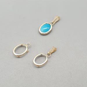 May include: Three gold-toned metal jewelry components consisting of two empty oval pendant settings and one oval pendant featuring a smooth, bright turquoise blue cabochon stone set within a matching gold-toned metal frame with a bail.
