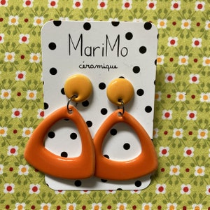 Puede incluir: Pendientes de cerámica naranja y amarillo con forma de triángulo y un agujero en el medio. Los pendientes están en una tarjeta blanca con lunares negros y el texto "MariMo céramique".