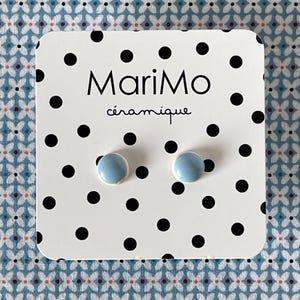 Peut inclure: Une paire de boucles d'oreilles à clous en céramique bleu clair, présentées sur une carte carrée blanche à pois noirs. La carte porte l'inscription MariMo céramique en lettres noires. Les boucles d'oreilles ont une finition lisse et brillante.