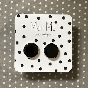 Può includere: Un paio di orecchini a bottone in ceramica nera su una carta bianca con pois neri. La carta riporta il testo "MariMo céramique".
