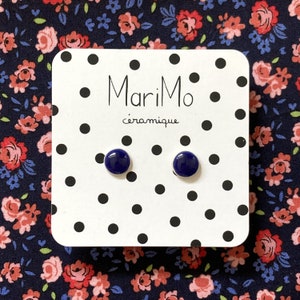 Puede incluir: Un par de pendientes de botón de cerámica azul sobre una tarjeta blanca con lunares negros. La tarjeta tiene el texto "MariMo céramique" impreso en ella.
