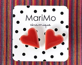 May include: A pair of glossy red heart-shaped ceramic stud earrings attached to a white display card with black polka dots. The card features the text MariMo céramique printed in black. The earrings have a smooth, reflective finish.