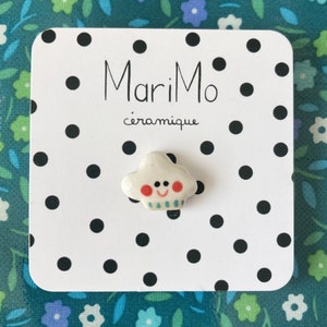 Peut inclure: Nuage en céramique blanche avec un visage souriant, des joues rouges et une écharpe rayée bleue et verte. Le nuage est sur une carte blanche avec des pois noirs et le texte "MariMo céramique".