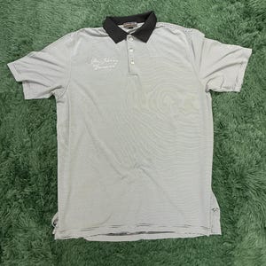 May include: Gray and white striped polo shirt with a black collar and three buttons. The shirt has short sleeves and a small embroidered logo on the sleeve. The text "Pure Luxury Genuine" is embroidered on the chest.