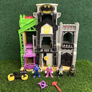Peut inclure: Un jeu Batman à plusieurs niveaux avec un Bat-Signal sur le dessus, comprenant une grue verte, une plate-forme violette et des portes noires. Comprend des figurines de Batman, du Joker et d'autres personnages, ainsi qu'une moto et des accessoires.
