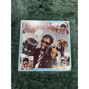May include: A square vinyl record cover featuring Bootsy's What's Bootsy? album art. The light blue cover displays multiple photographs of a person wearing sunglasses and a top hat, with comic-style speech bubbles containing text like That Will Work.