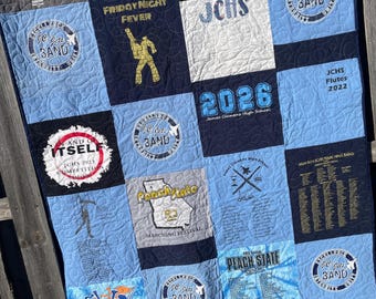 May include: A blue and black patchwork quilt made from t-shirts. The quilt features the names of a high school marching band, including "James Clemens High School", "Peach State Marching Festival", and "JCHS Jets Band".