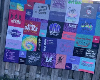 May include: A quilt made of t-shirts with dance-themed designs. The quilt is made up of many different colors, including purple, blue, pink, and green. The quilt features text such as "Company Dancer", "Born to Dance", "Athlete Artist", "It's a good day to dance", and "ASD Company Dancer".