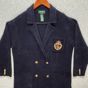 May include: Navy blue corduroy blazer with gold-colored buttons and a crest on the pocket. The blazer has a double-breasted design and a classic lapel. The brand label is visible on the collar.
