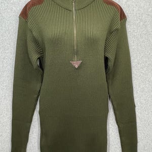 May include: An olive green ribbed knit sweater with a half-zip and brown suede shoulder patches. The long-sleeved sweater features a small leather triangle detail at the zip. The garment is displayed on a white mannequin.