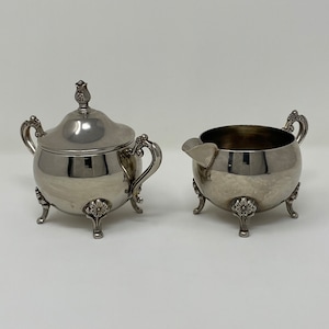 May include: A silver sugar bowl and creamer set with ornate handles and feet. The pieces have a classic, elegant design.