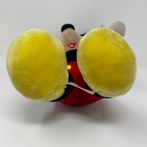 May include: A plush Mickey Mouse toy with red shorts, yellow shoes, and black eyes. The toy is lying on its back with its feet in the air.