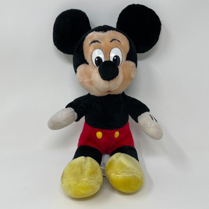 May include: A plush Mickey Mouse toy with black ears, a black body, red shorts with yellow buttons, and yellow shoes.