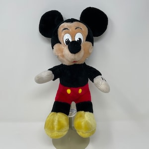 May include: A black and red plush Mickey Mouse toy with yellow shoes. The toy has a black nose and large, white eyes.