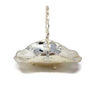 May include: A silver serving basket with a twisted handle and a decorative, scalloped edge. The basket has a delicate, floral design.