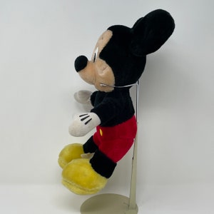 May include: A black and red plush Mickey Mouse toy with yellow shoes. The toy is standing on a metal stand.