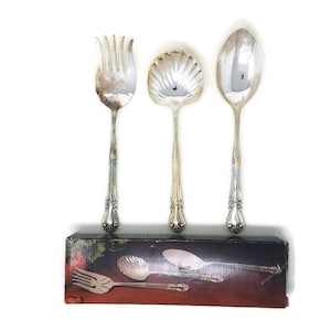 Könnte beinhalten: Ein Set aus drei versilberten Servierbesteck, bestehend aus einer Gabel, einem Servierlöffel und einer Schöpfkelle. Das Besteck hat verzierte Griffe und befindet sich in einer Schachtel.